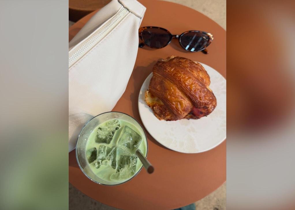 An iced matcha and a ham and Swiss croissant on a round terracotta table, seen from above