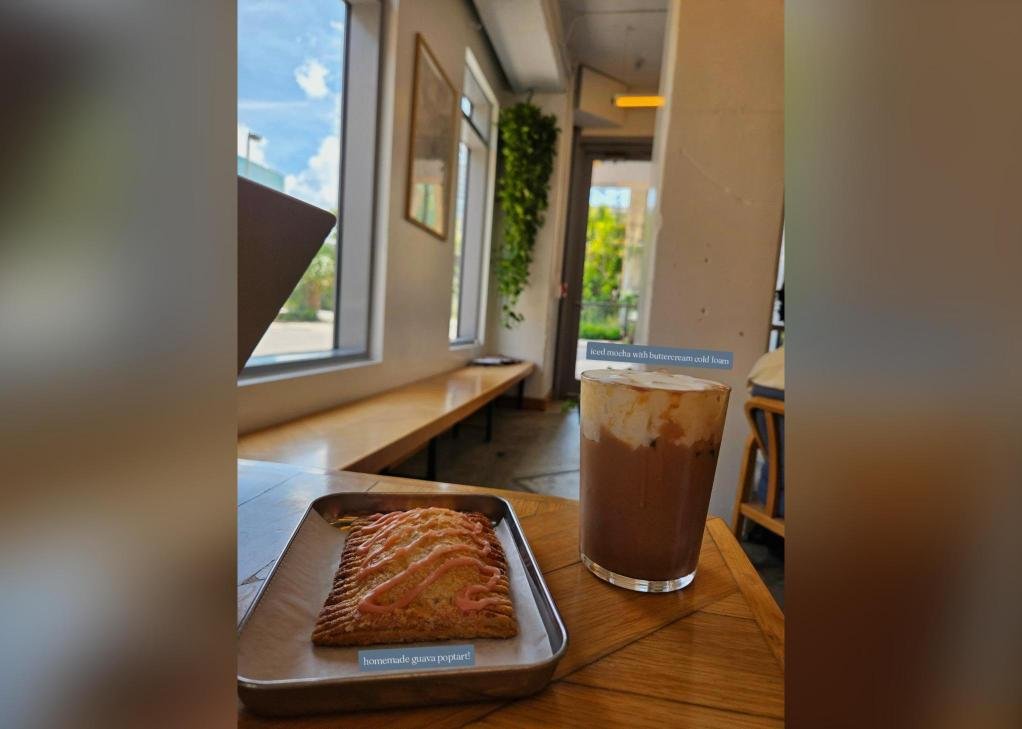 A homemade guava pop-tart on a metal tray next to an iced mocha with cold foam by a sunny window