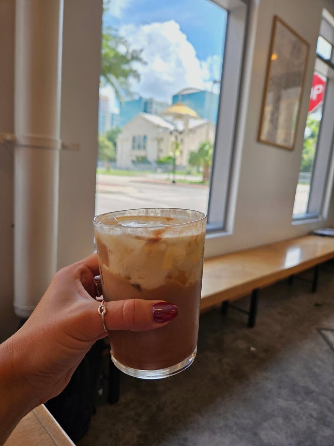 A homemade guava pop-tart on a metal tray next to an iced mocha with cold foam by a sunny window